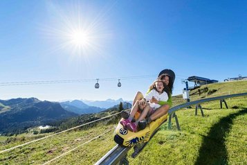 Mutter und Tochter fahren auf einem Sommerrodel durch die Berglandschaft und genießen das Abenteuer nahe des Familienhotels Ramsi in Kärnten