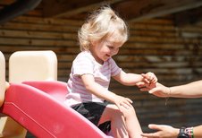 Kleines Kind rutscht lachend eine rote Rutsche hinunter und wird von einer Betreuerin im Familienhotel Sonne Bezau aufgefangen.