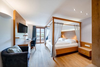 Zimmer mit Himmelbett, Schreibtisch, Fernseher und Zugang zum Balkon mit Bergblick im Familienhotel Amiamo.