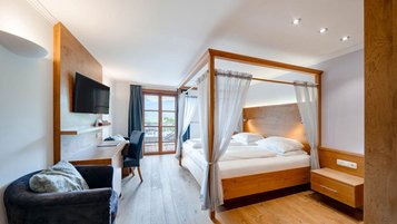 Zimmer mit Himmelbett, Schreibtisch, Fernseher und Zugang zum Balkon mit Bergblick im Familienhotel Amiamo.
