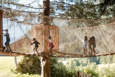 Kinder balancieren über eine Hängebrücke im Waldspielbereich des Familienhotels Huber in Südtirol
