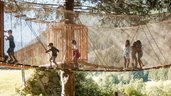 Kinder balancieren über eine Hängebrücke im Waldspielbereich des Familienhotels Huber in Südtirol