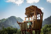 Kinder stehen lachend auf einem hölzernen Aussichtsturm mit Bergblick am Waldspielplatz des Familienhotels Krone im Allgäu.
