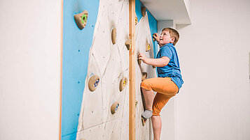 Junge klettert an der Indoor Kletterwand im Happy-Club des Familienhotels Landgut Furtherwirt in Tirol.