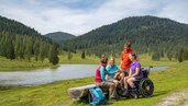 Landschaftsbild von Kaernten und einer Familie. Die Strecke ist barrierefrei und bietet eine tolle Sicht auf einen See.
