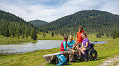 Landschaftsbild von Kaernten und einer Familie. Die Strecke ist barrierefrei und bietet eine tolle Sicht auf einen See.