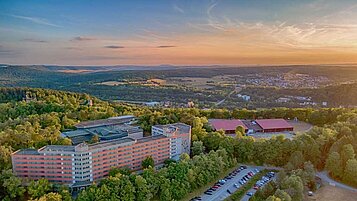 Luftaufnahme des Familienhotels Sonnenhügel bei Sonnenuntergang, eingebettet in die idyllische Landschaft des Bayerischen Waldes mit umgebenden Wäldern und sanften Hügeln.