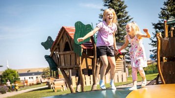 Zwei Mädchen hüpfen fröhlich auf einem riesigen Luftkissen im Outdoor-Spielbereich des Elldus Resorts im Erzgebirge