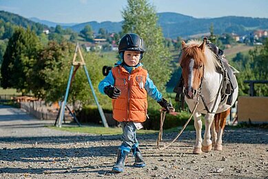 Kleiner Junge führt ein Pony auf dem Außengelände des Familienhotels Landhaus zur Ohe an der Leine.