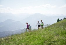 Familie wandert über eine grüne Bergwiese mit weitem Blick auf die Alpen beim Familienhotel Sonne Bezau.