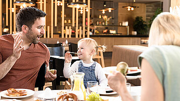 Vater und Kind sitzen am gedeckten Frühstückstisch im Familienhotel.
