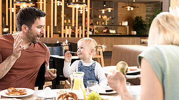 Vater und Kind sitzen am gedeckten Frühstückstisch im Familienhotel.