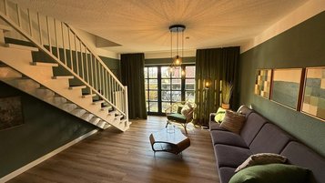 Wohnbereich mit gemütlichem Sofa, Treppe zur Galerie und direktem Zugang zur Terrasse im Familienhotel Gut Landegge