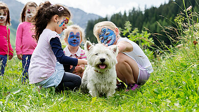 Kinder mit bemalten Gesichtern streicheln einen Hund im Familienhotel Kaiserhof an der Tiroler Zugspitzarena.