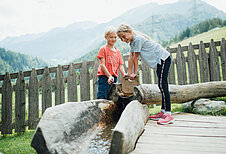 Ein Junge und ein Mädchen spielen auf der Abenteuerspielwiese des Kinderhotels Sailer mit Wasser.