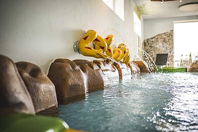 Kinderbecken im Hotel mit wasserspeienden Clownfisch-Figuren an der Wand, die in ein warmes, sprudelndes Becken münden, für eine spielerische und kinderfreundliche Badeerfahrung.