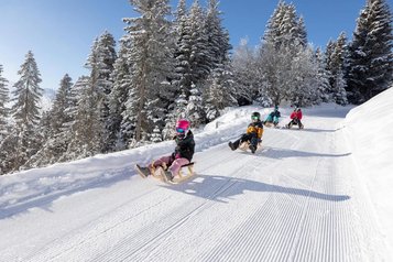 Kinder rodeln die Piste hinunter in Serfaus-Fiss-Ladis in der Nähe vom Familienhotel Adler Familien- & Wohlfühlhotel.