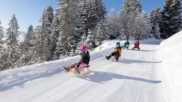 Kinder rodeln die Piste hinunter in Serfaus-Fiss-Ladis in der Nähe vom Familienhotel Adler Familien- & Wohlfühlhotel.