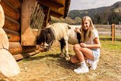 Mädchen streichelt ein Pony vor einer Almhütte im Familienhotel Scherer.