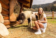 Mädchen streichelt ein Pony vor einer Almhütte im Familienhotel Scherer.