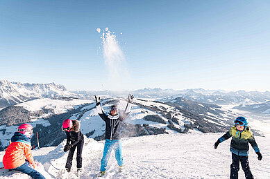 Eine Familie macht eine kurze Pause und bewirft sich mit Schnee auf der Piste nahe des Familienhotels Das Hopfgarten in Tirol.