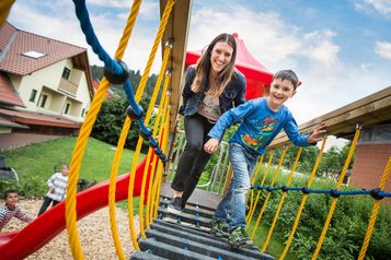 Mutter und Sohn spielen lachend auf einer Hängebrücke am Spielplatz des Familienhotel Ottonenhof.