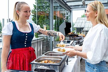 Eine freundliche Kellnerin in Tracht bedient einen Hotelgast des Hotels Alpengasthof Hochegger am bunten Grillbuffet.