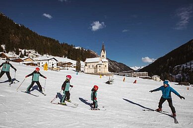 Kinder der Kinderskischule fahren mit ihrem Lehrer die Piste hinunter in der Nähe vom Familienhotel Bella Vista in Südtirol.