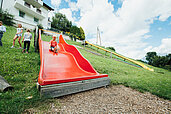 Junge rutscht eine große rote Rutsche auf der Abenteuerspielwiese des Kinderhotels Sailers hinab.