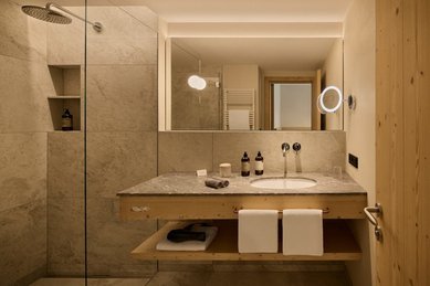 Modernes Badezimmer im Hotel Bella Vista in Südtirol mit Waschbecken, großer Spiegelwand und Dusche.