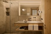 Modernes Badezimmer im Hotel Bella Vista in Südtirol mit Waschbecken, großer Spiegelwand und Dusche.