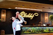 Mutter hält ihr Baby mit den Händen in die Höhe vor der Rezeption des Familienhotels Ulrichshof im Bayerischen Wald.