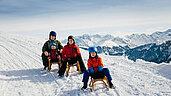 Familie beim Schlittenfahren im Winterurlaub in Vorarlberg.